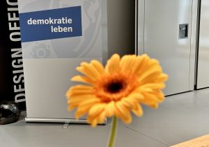 Gelbe Blume vor einem Aufsteller mit Aufdruck: Demokratie leben