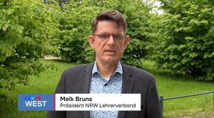 Ein Mann mit Brille, buntem Hemd und Sakko steht im Grünen und spricht in eine Kamera.